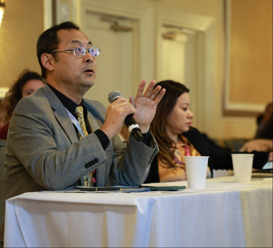 Dr. Guangrong Lu taking part in a scientific discussion with a handheld microphone at ET-19.