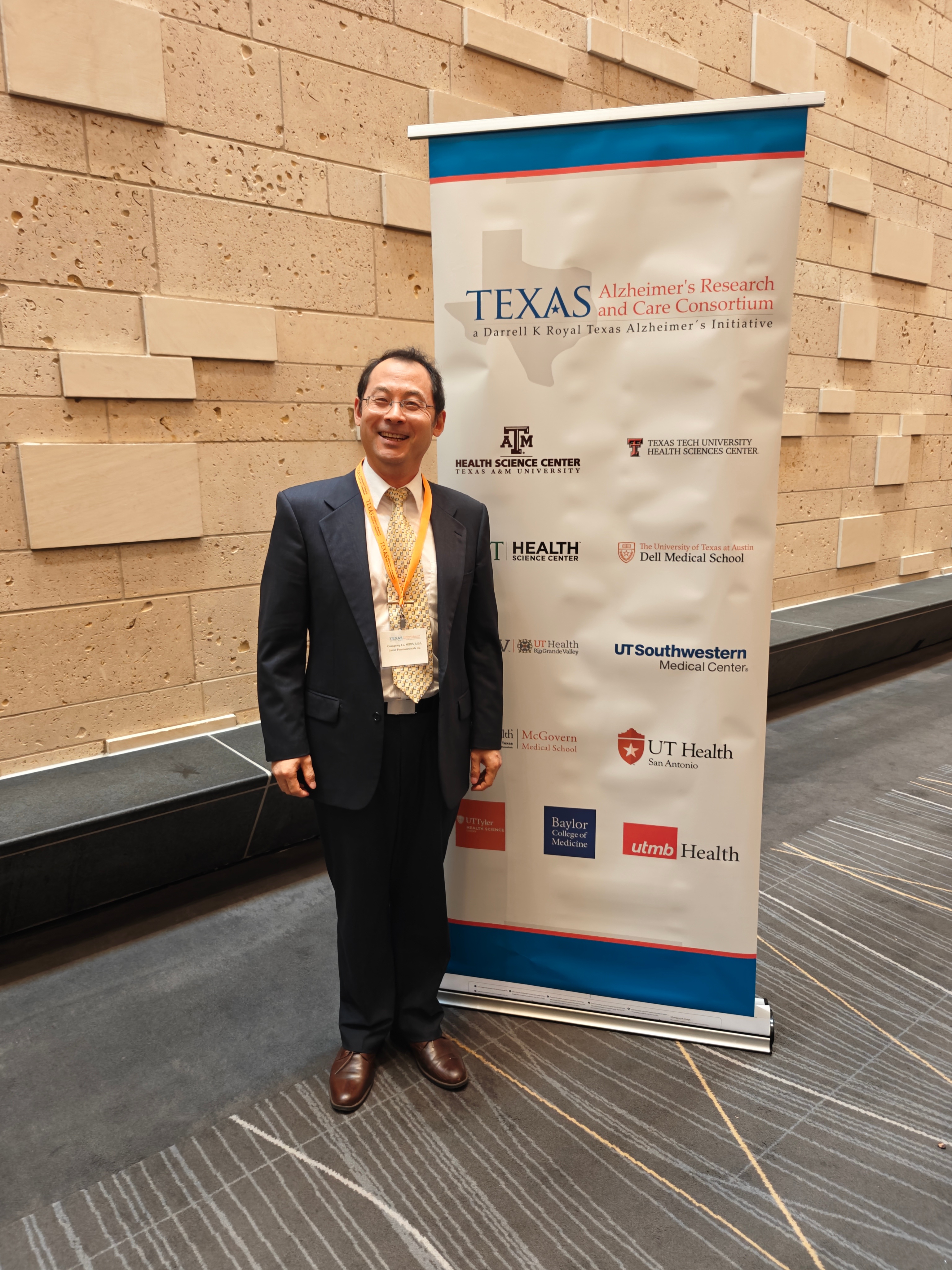 Dr. Guangrong Lu beside the Texas Alzheimer’s Research and Care Consortium banner.